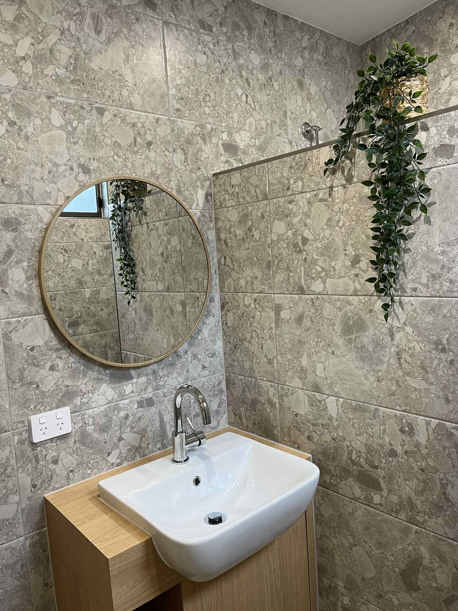 Ein Badezimmer mit rundem Spiegel, einem weißen Waschbecken und einer Wandpflanze.