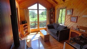 Ein gemütliches Blockhaus mit Holzvertäfelung, einer Couch, einem Esstisch und Blick ins Freie.