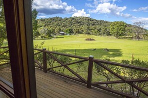 A wooden deck with a view of a grassy field and a hill in the background. - Wisteria Cottage and Cabins (Wyberba)
