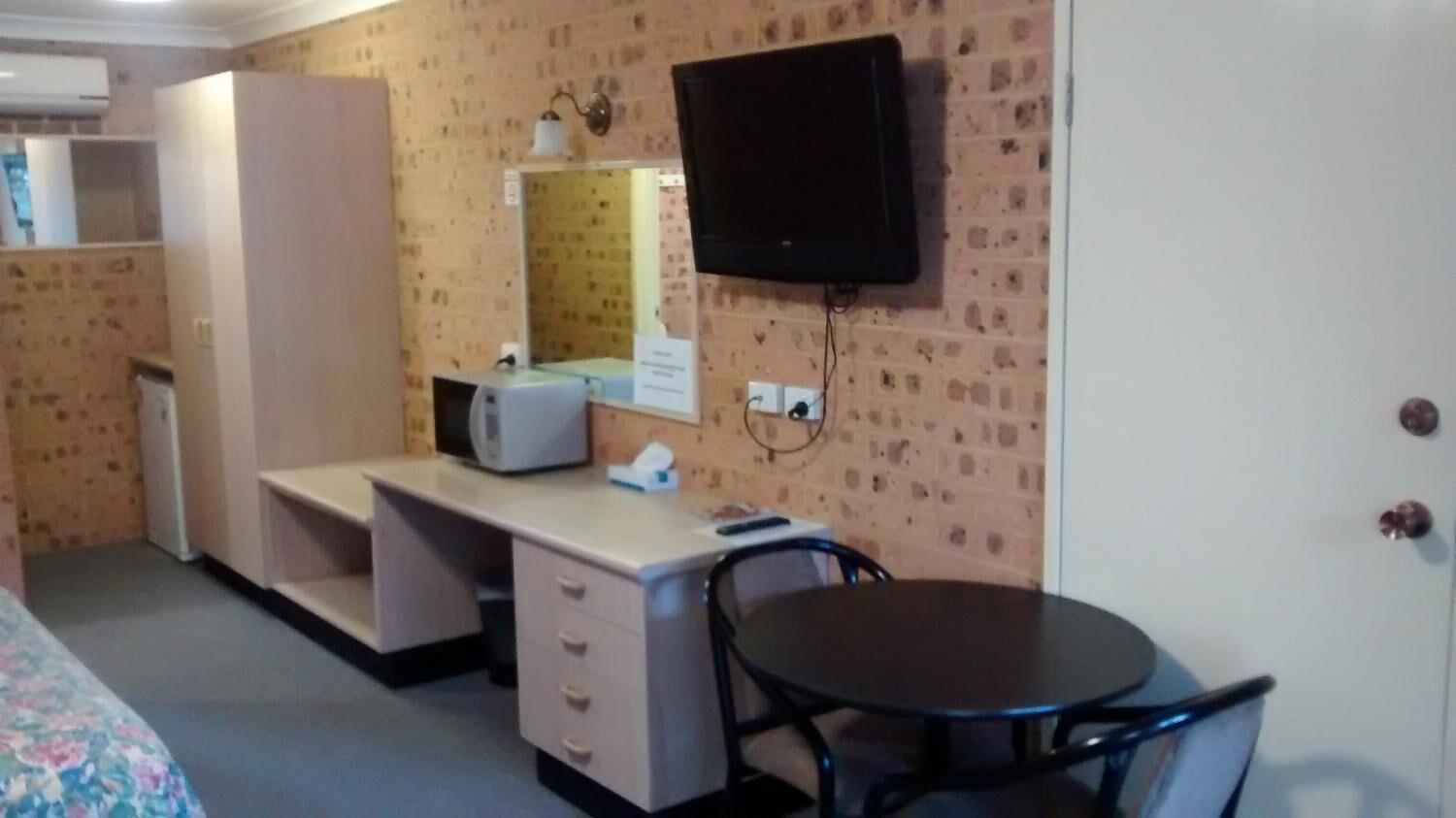 Une pièce comprenant un lit, un bureau avec une chaise, un téléviseur fixé au mur et une petite table.