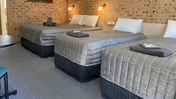 A hotel room with two beds, a small table, and a brick-patterned wall.