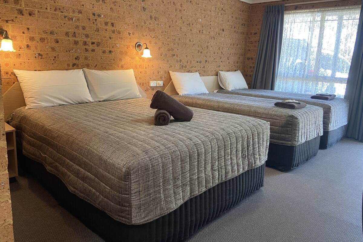 A hotel room with two beds, a brick wall, and a window with curtains.