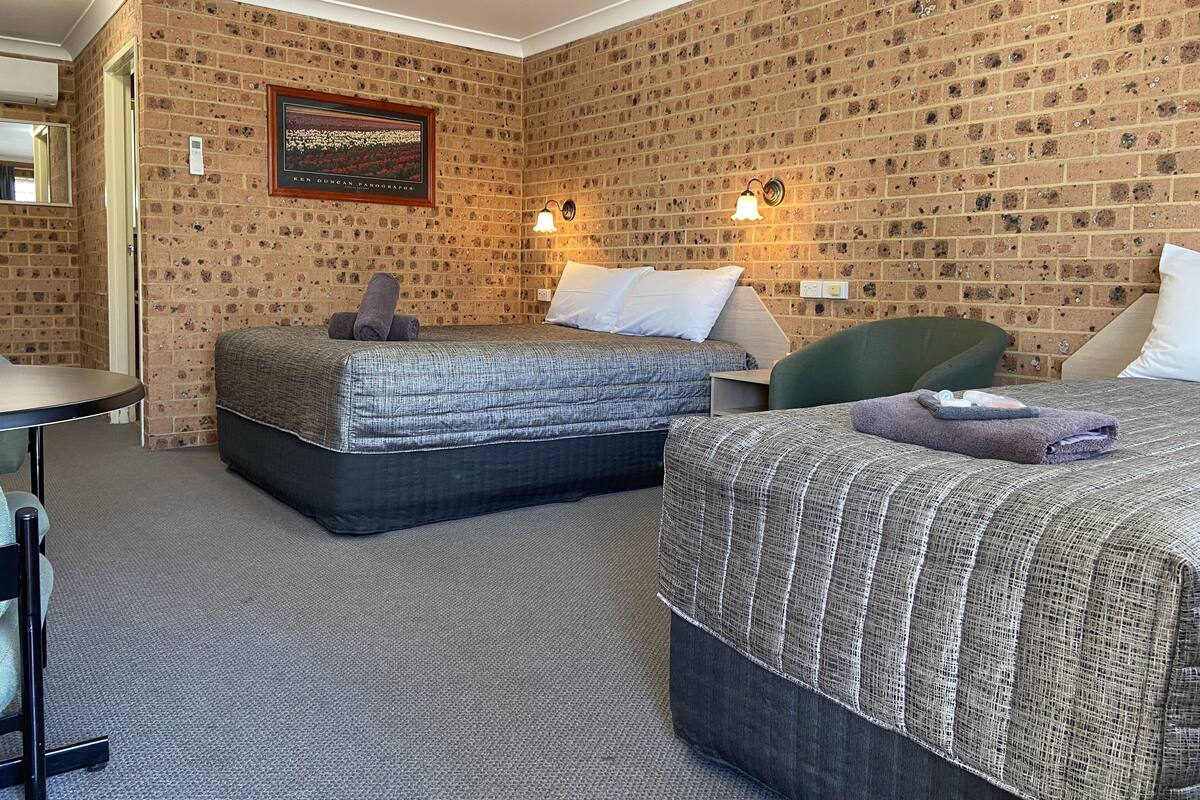 A hotel room with two beds, a small table, and a green chair.