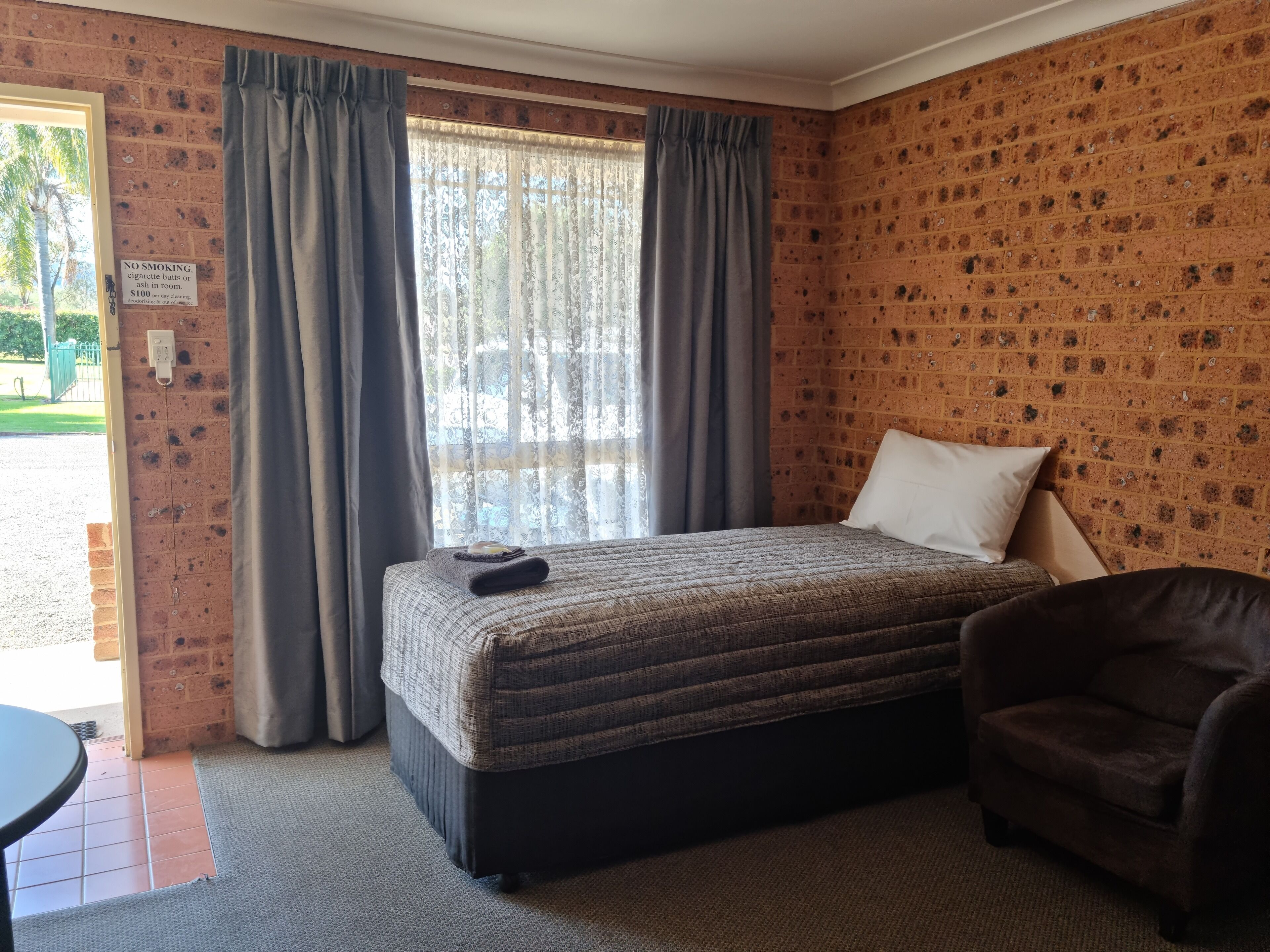 Una habitación con cama, una silla y un ventanal con cortinas.