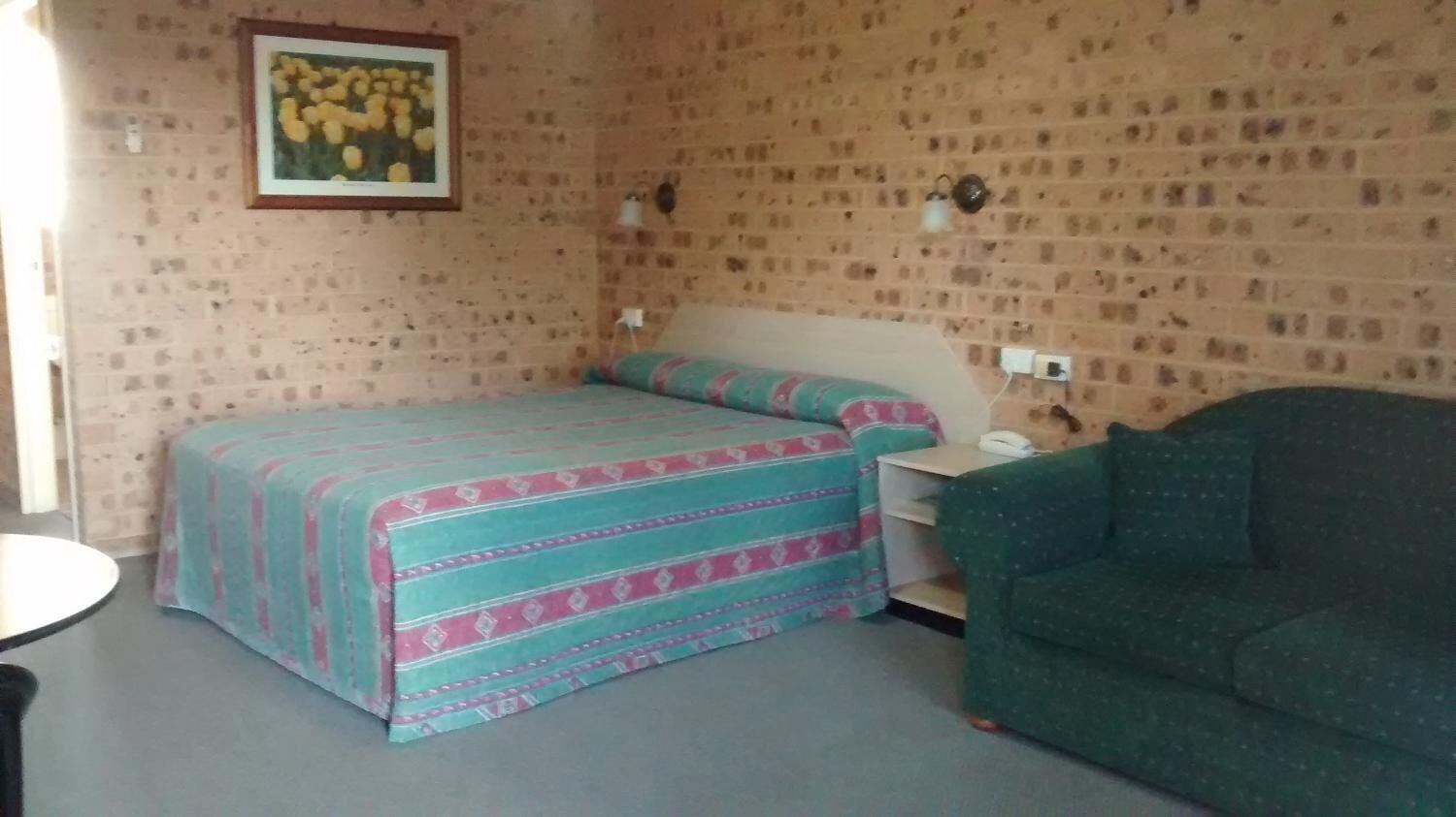 A room with a bed, a green sofa, a small table, and a wall-mounted telephone.