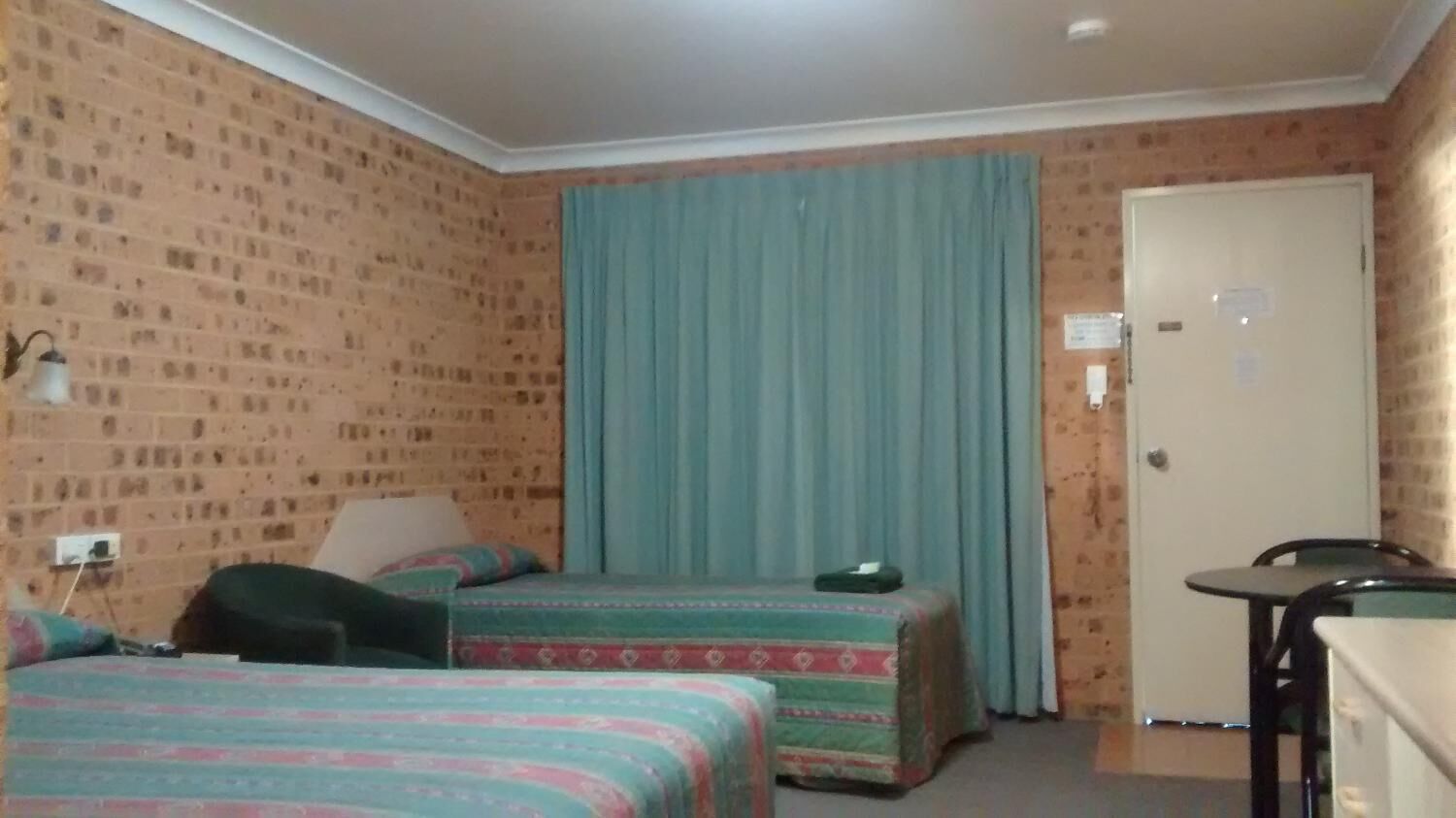 A room with two beds, a desk, a chair, a door, and a window with curtains.