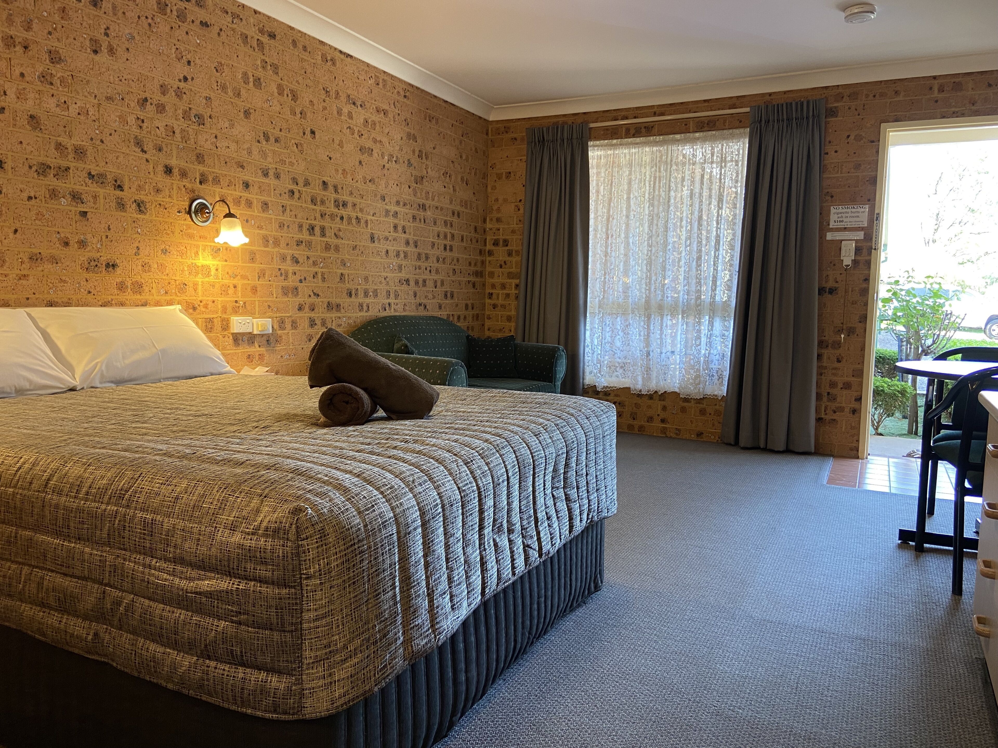A hotel room with a large bed, a chair, a table, and a window with curtains.