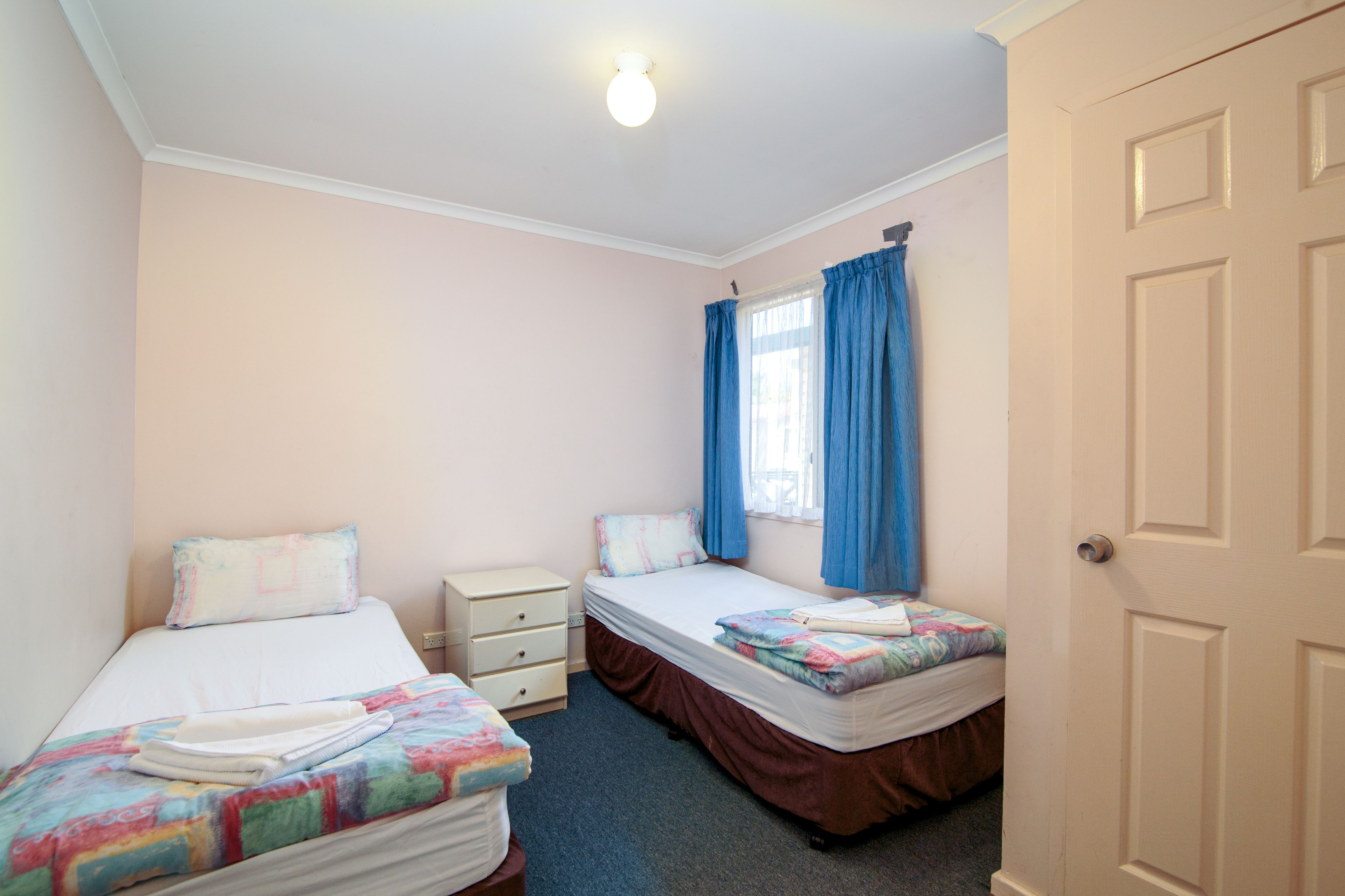 A bedroom with two single beds, a nightstand, a dresser, and a window with blue curtains.