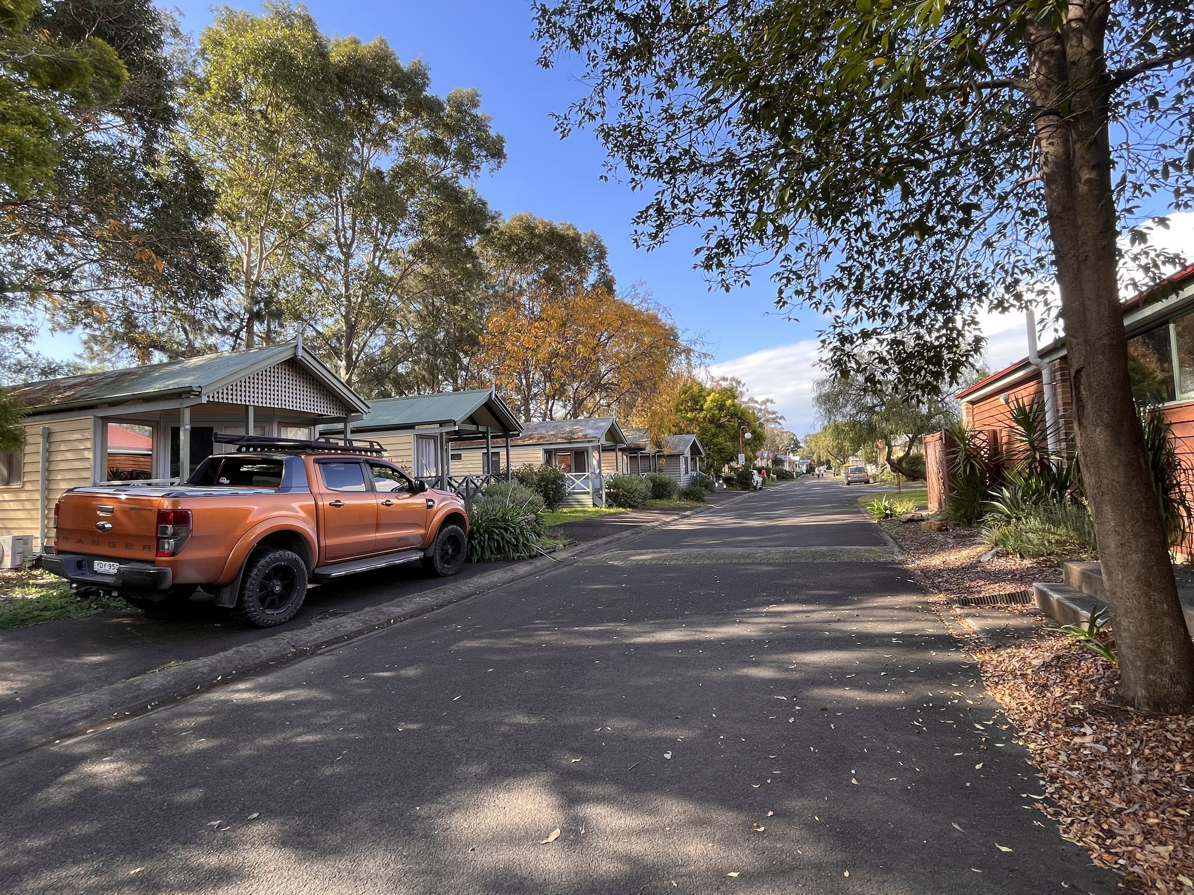 Una calle residencial con casas, una camioneta naranja estacionada y árboles.