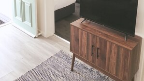 Ett sovrum med en säng, en tv-apparat placerad på ett träskåp, en dörr med ett blommönster och en målning av träd på väggen.