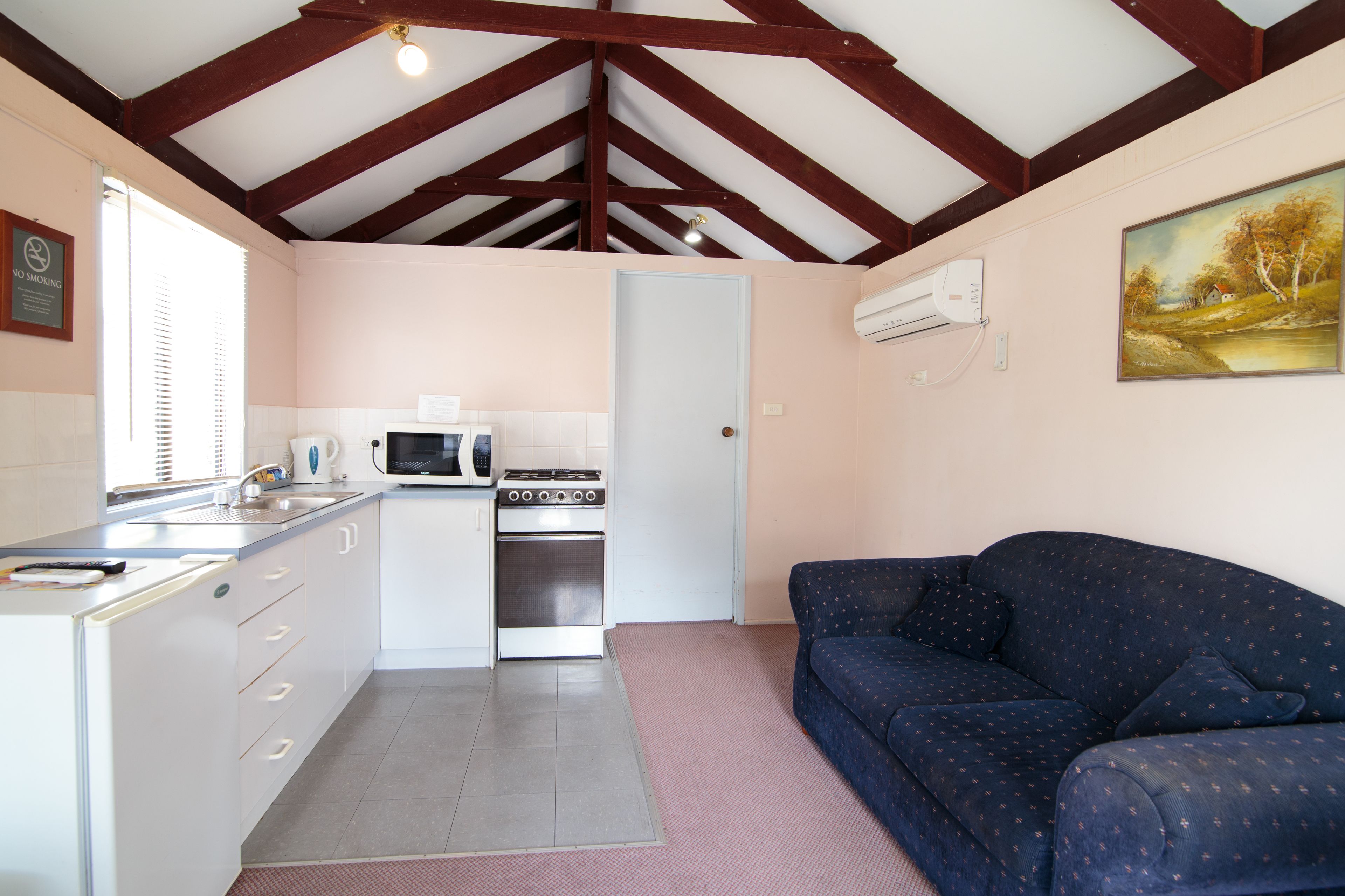 A compact kitchen with a microwave, stove, and sink, a blue sofa, and a painting on the wall.