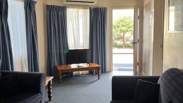 Ein Wohnzimmer mit zwei Sofas, einem Couchtisch und einem Fernseher. Eine Klimaanlage ist an der Decke angebracht.
