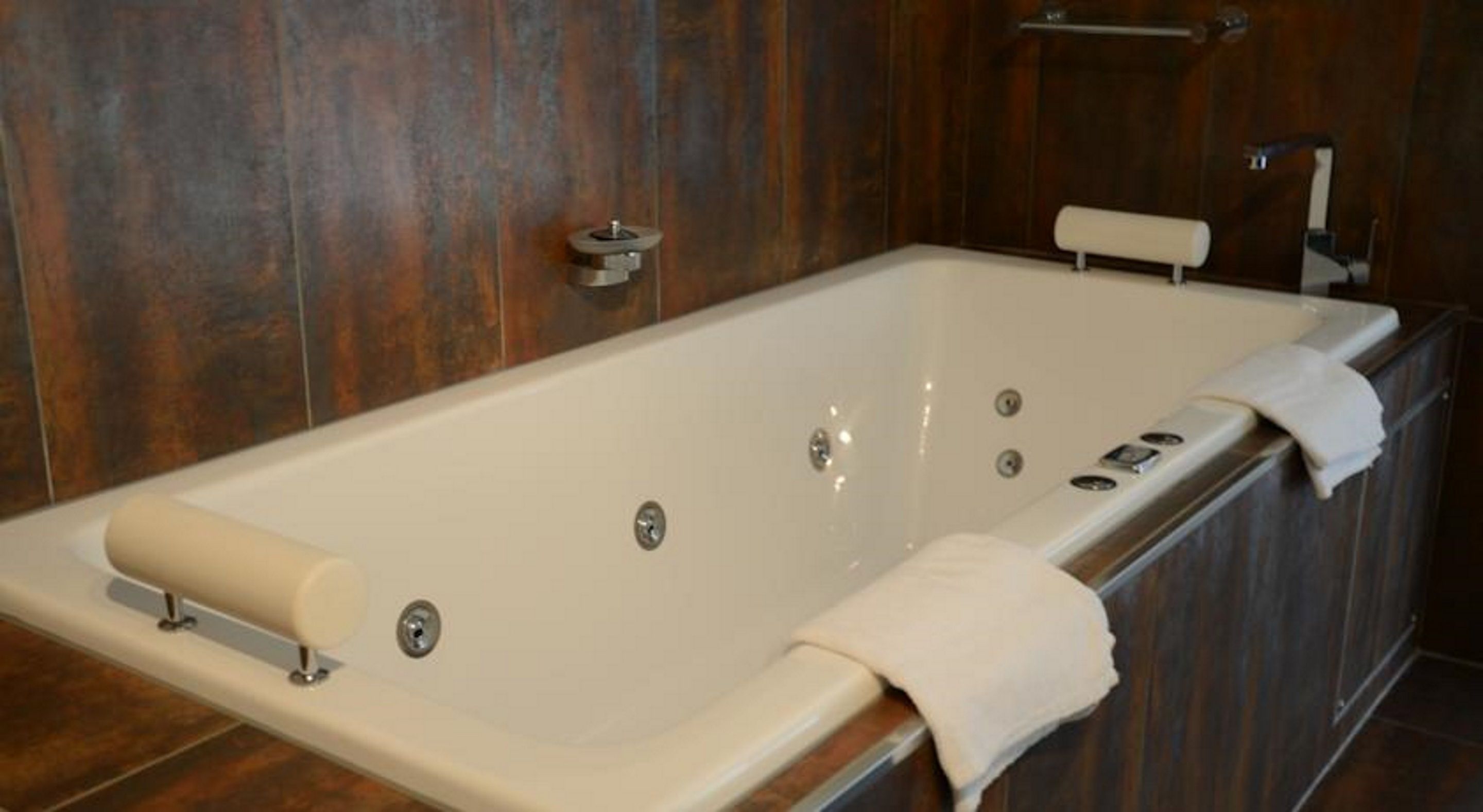 Eine große, rechteckige Badewanne mit weißem Innenraum vor einer Holzwand.