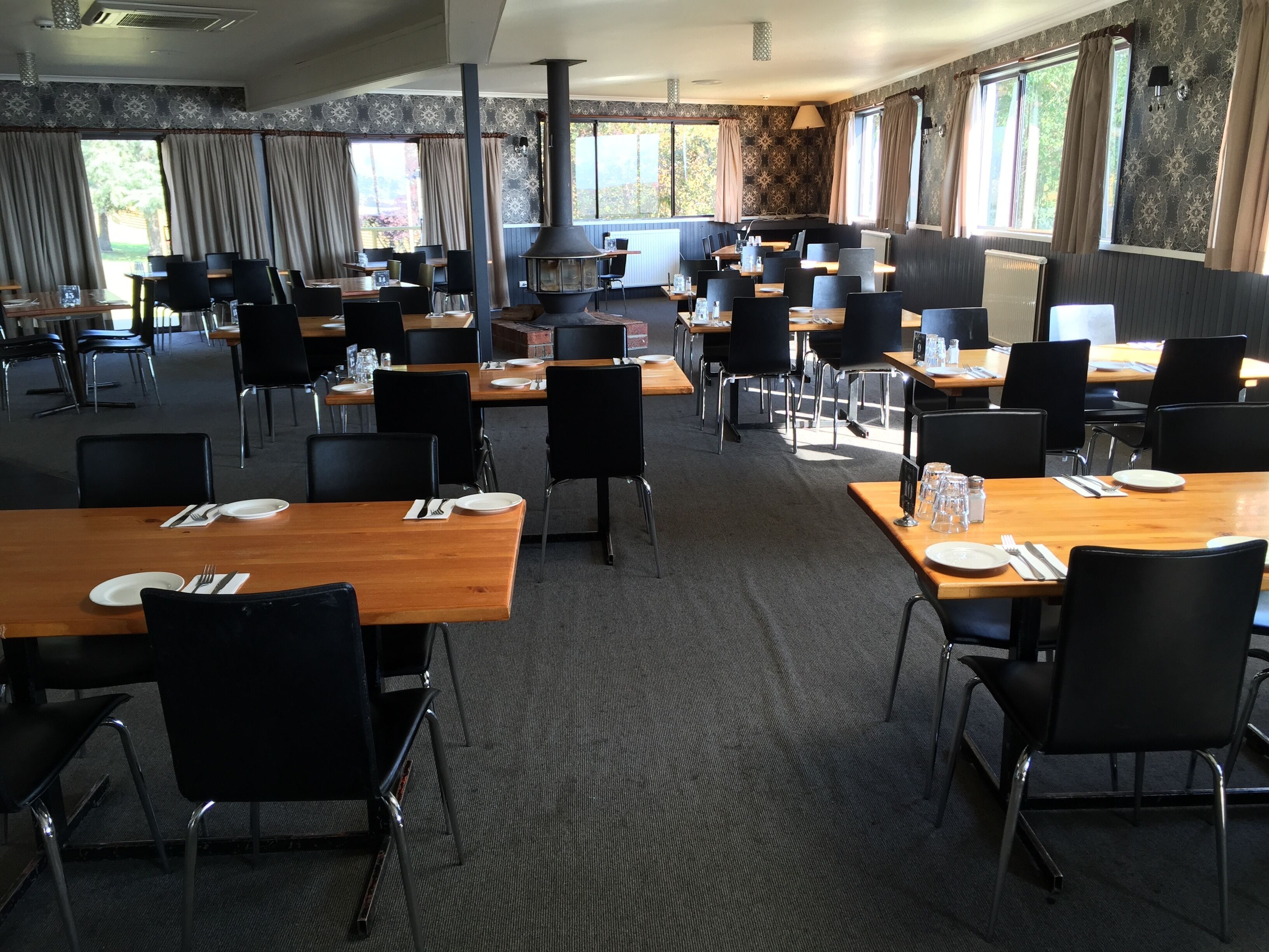A spacious dining area with multiple tables and chairs, large windows with curtains, and a central fireplace.