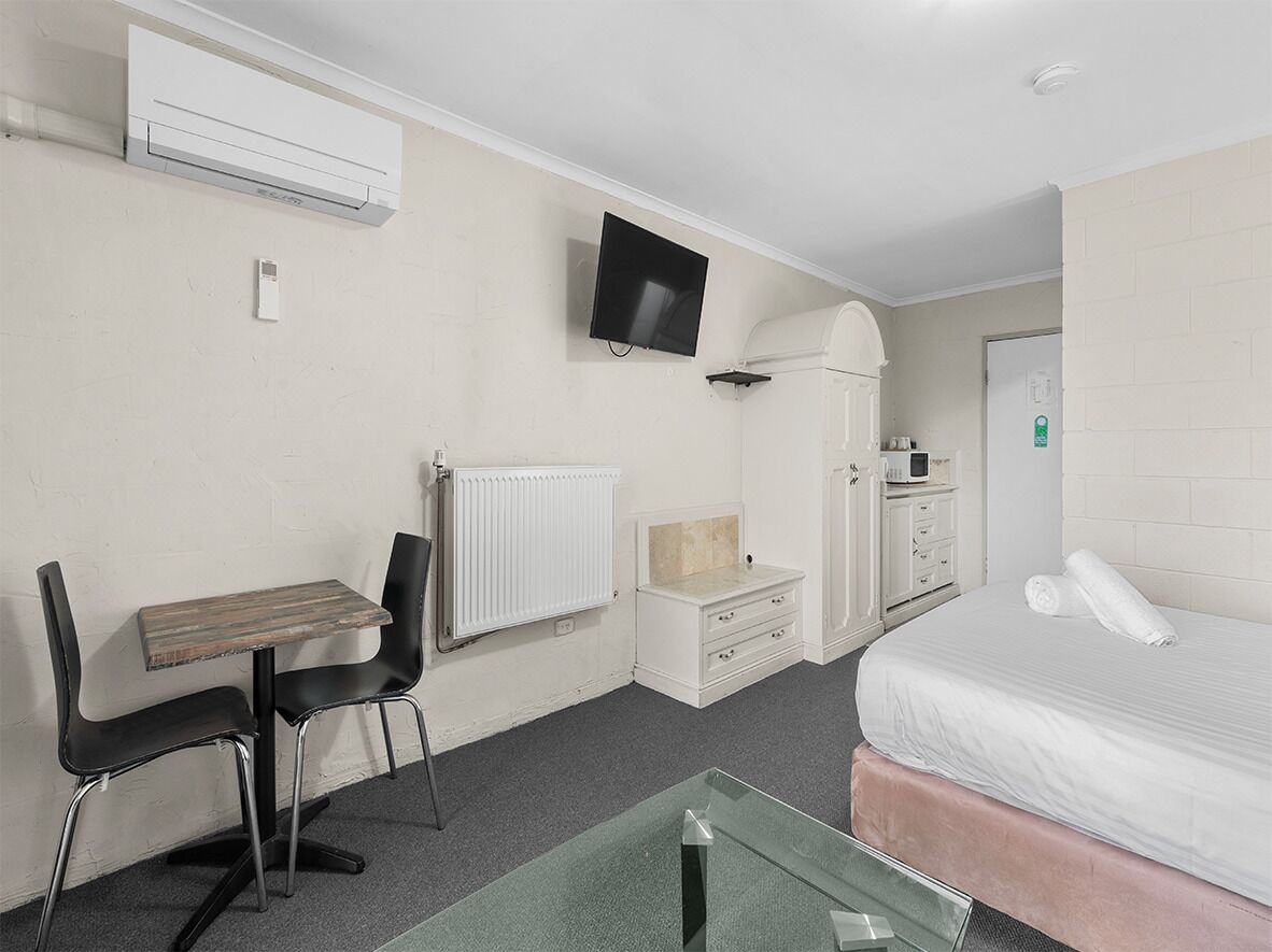 A hotel room with a bed, a desk with two chairs, a television, a radiator, a wardrobe, and a small table.