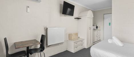 A hotel room with a bed, a desk with two chairs, a television, a radiator, a wardrobe, and a small table.