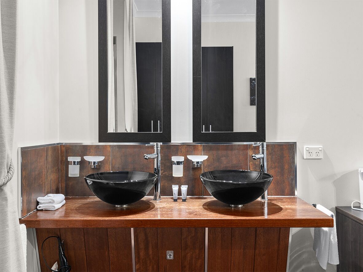 A bathroom with two black vessel sinks, a wooden vanity, and a large mirror above the sinks.