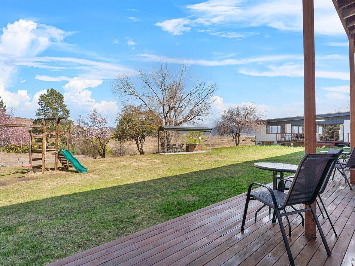 A wooden deck with outdoor seating, a playground, and a grassy yard with trees.