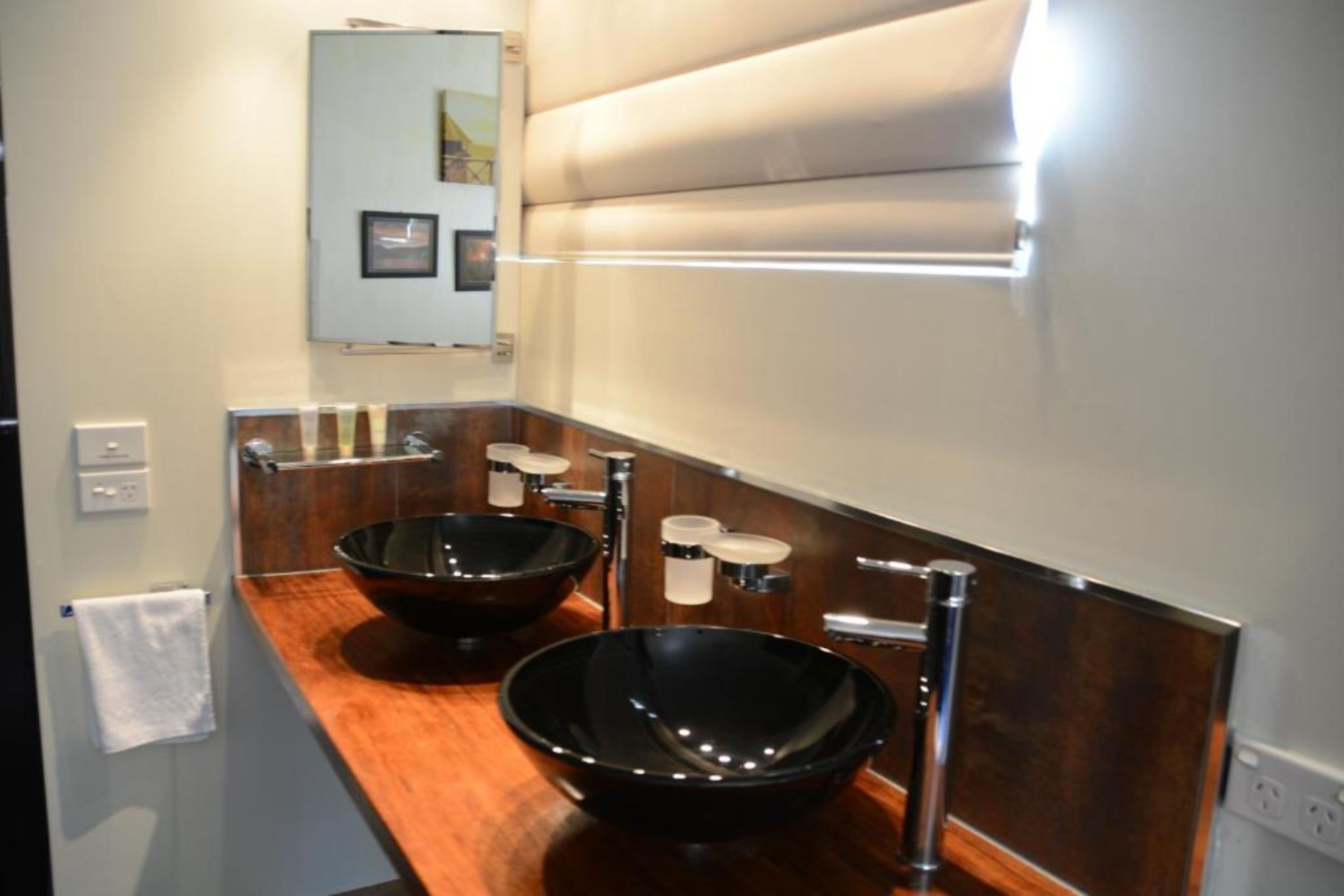 Een moderne badkamer met twee zwarte wastafels, een houten aanrechtblad en een spiegel boven de wastafel.
