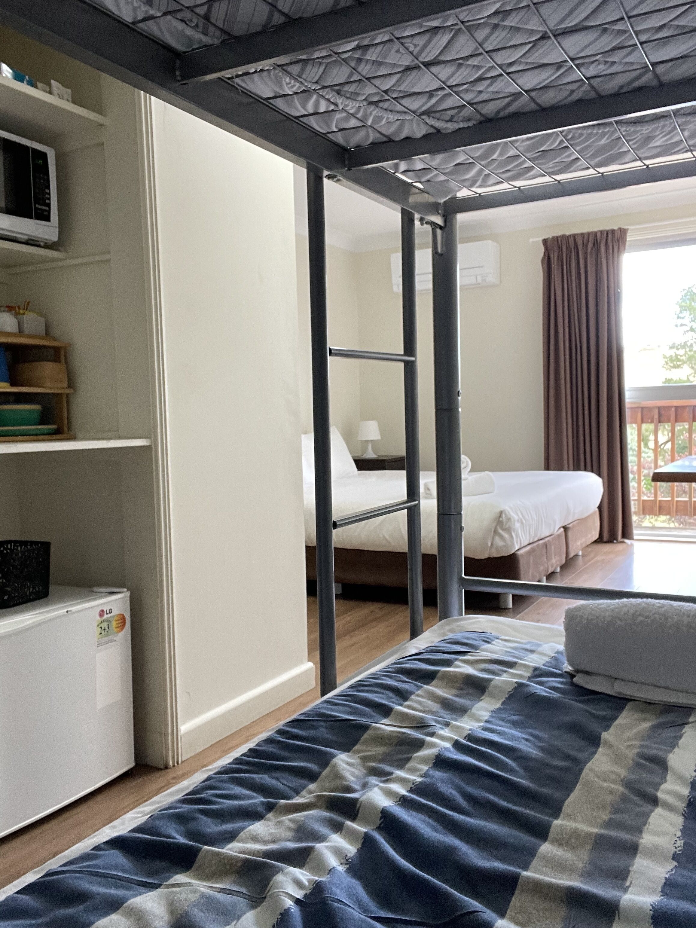 A bedroom with a bed, a wardrobe, a desk, and a window with curtains.