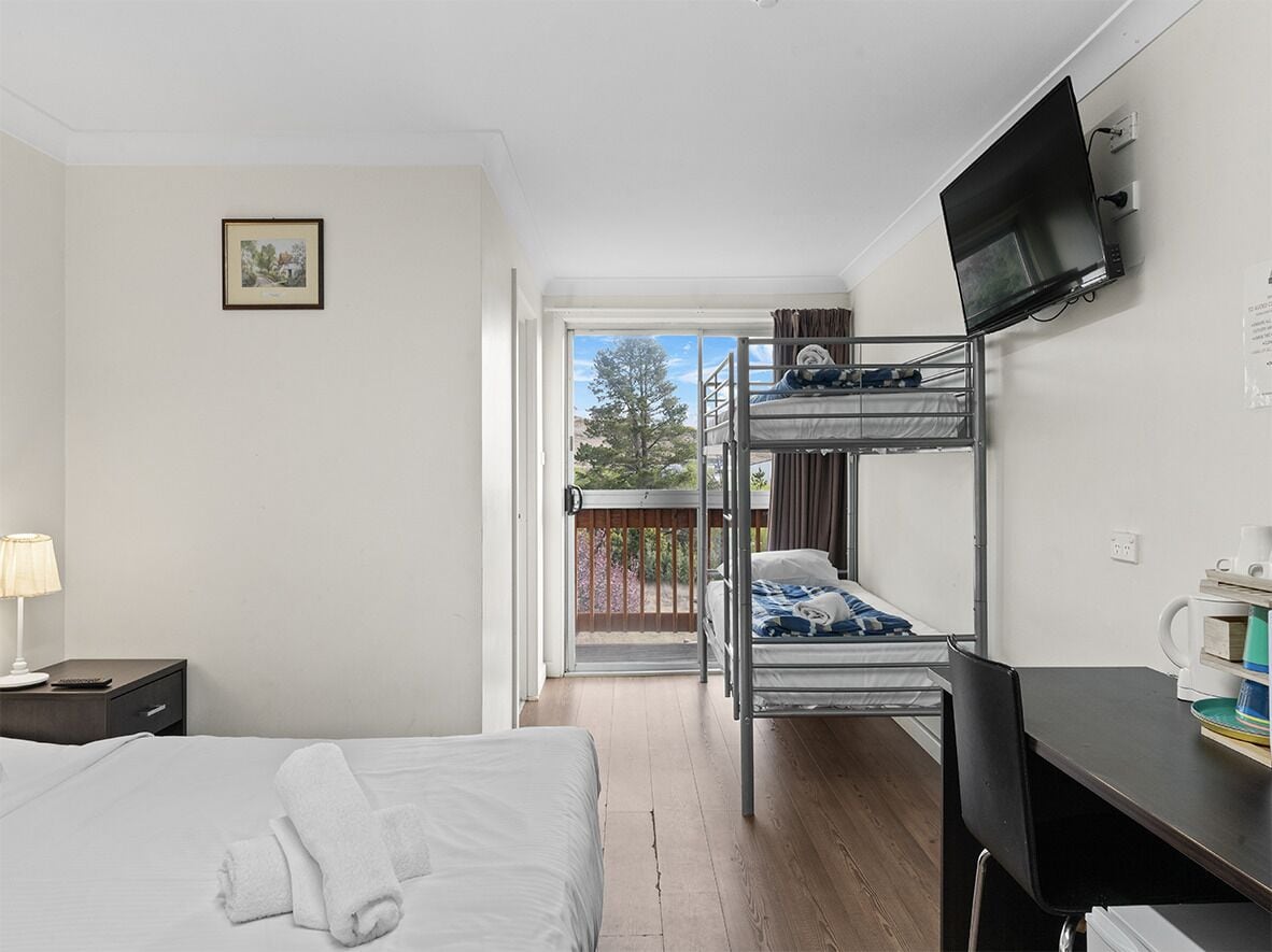 Hotelkamer met een bed, bureau, televisie en balkon met uitzicht op bomen.