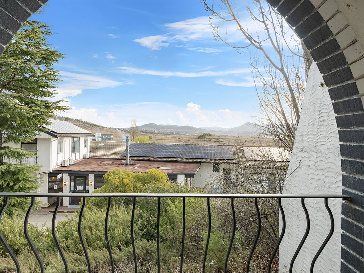 A balcony with a view of a residential area, including houses and distant hills.