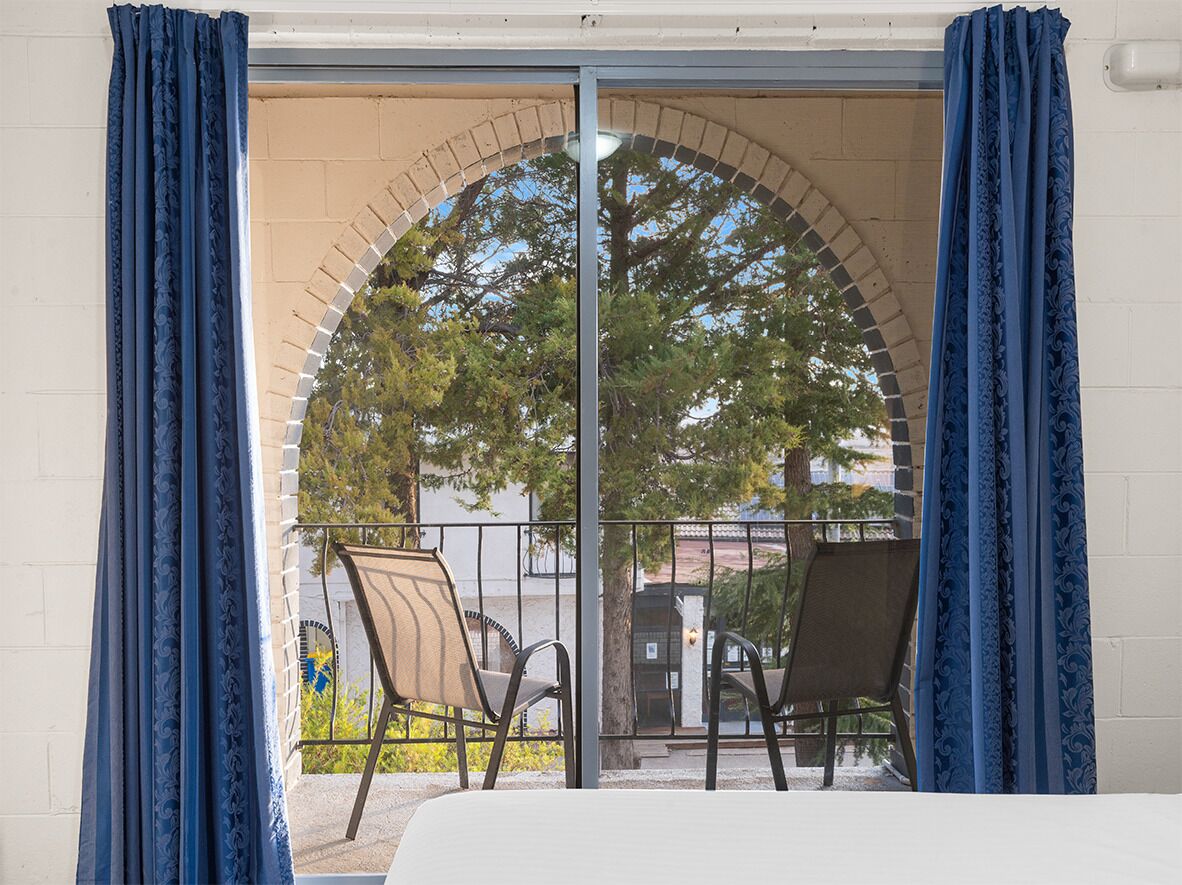 A balcony with two chairs, a view of trees, and a brick archway.