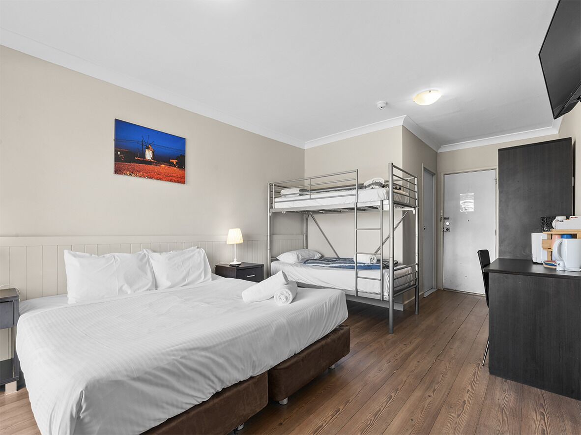 Habitación de hotel con literas, un escritorio, una silla, una lámpara y un cuadro en la pared.