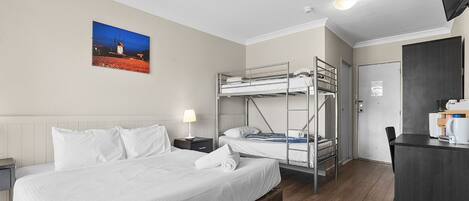Habitación de hotel con literas, un escritorio, una silla, una lámpara y un cuadro en la pared.