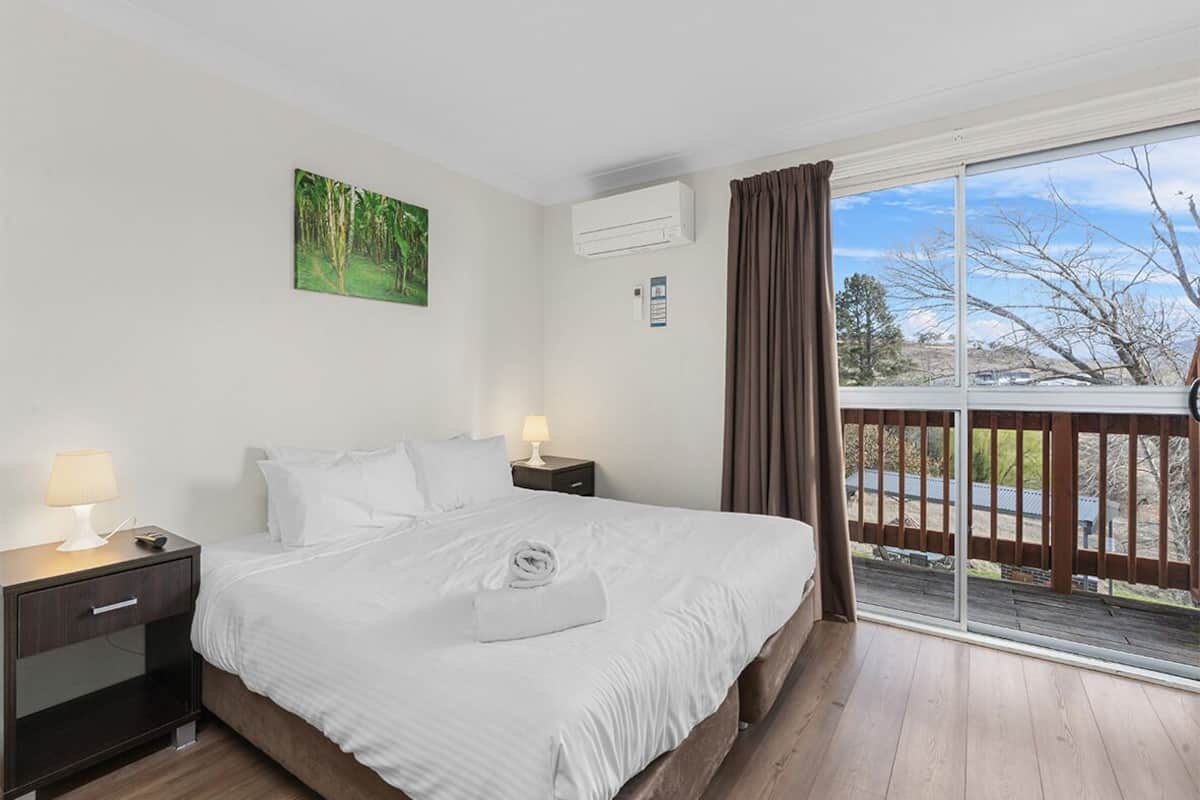 A hotel room with a bed, nightstands, a painting, an air conditioning unit, and a balcony with a view.