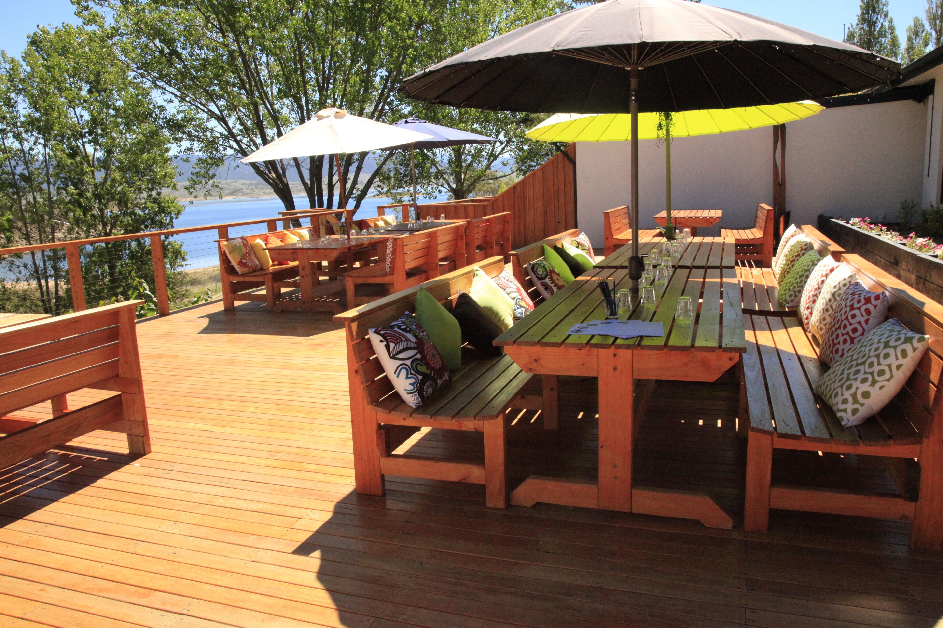 Une terrasse extérieure aménagée avec du mobilier en bois, notamment des bancs et une table, ainsi que des parasols pour créer de l’ombre.