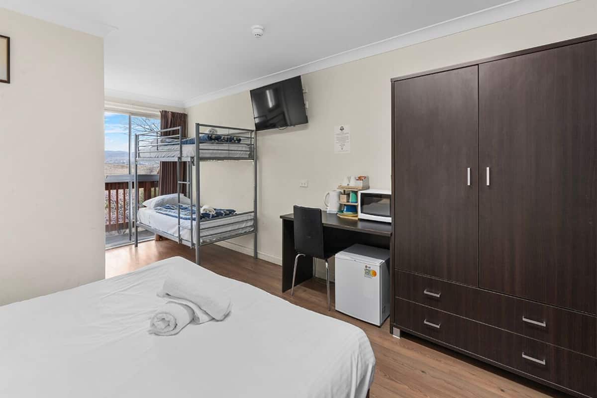 A hotel room with a bunk bed, a desk with a computer, a wardrobe, and a view of the outdoors.