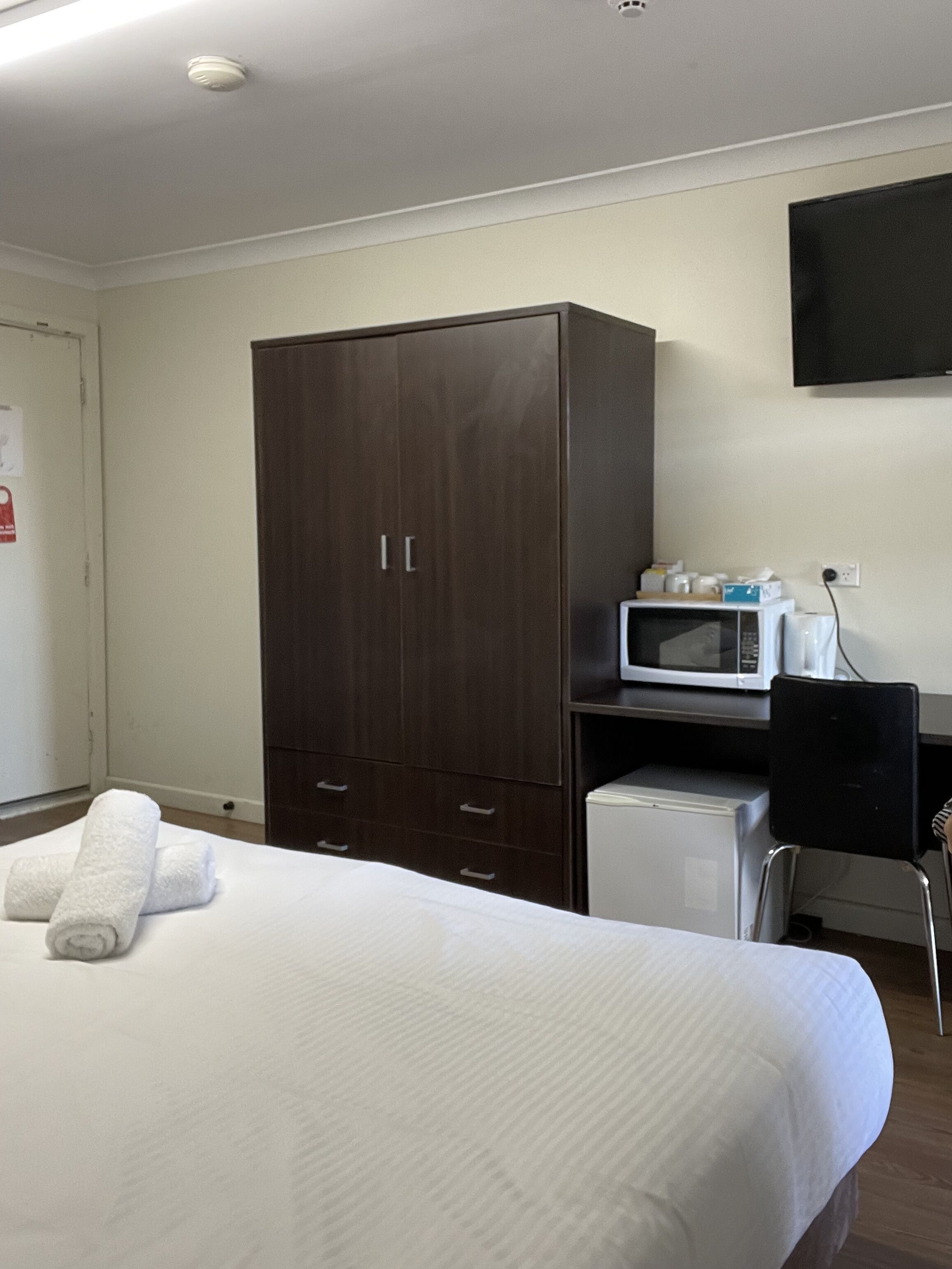 Habitación de hotel con cama, armario, microondas, pequeño refrigerador y televisión en la pared.