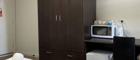 Ein Hotelzimmer mit Bett, Schrank, Mikrowelle, kleinem Kühlschrank und Fernseher an der Wand.