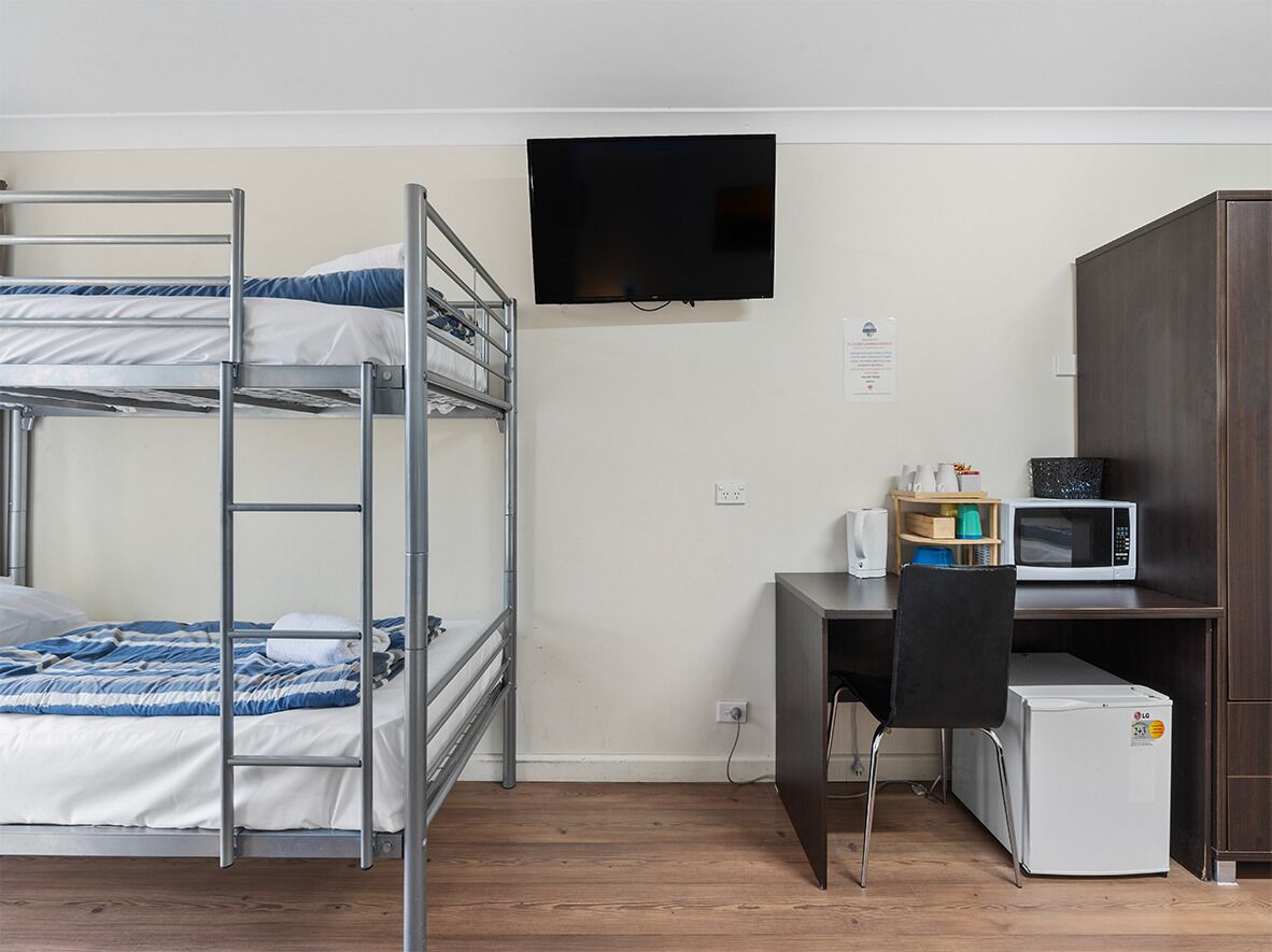 A bunk bed with a TV above it, a desk with a chair, a microwave, and a refrigerator.