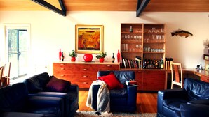 A living room with two blue sofas, a wooden cabinet with glassware, a painting, and a fish decoration on the wall. - Blue Lake Lodge (Arthurs Lake)