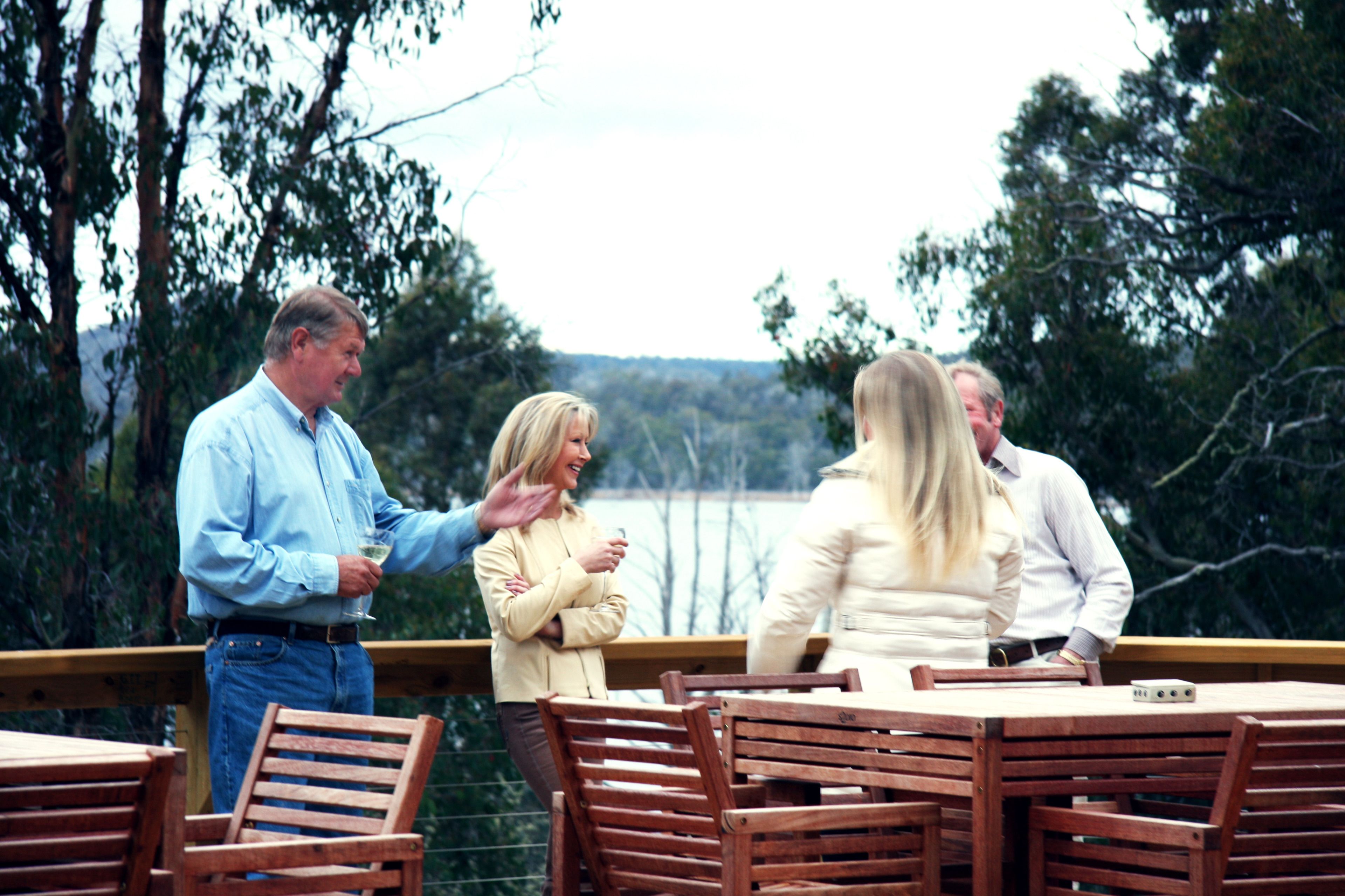 A group of people standing on a wooden deck with a table and chairs, overlooking a body of water and trees.