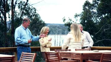 A group of people standing on a wooden deck with a table and chairs, overlooking a body of water and trees.