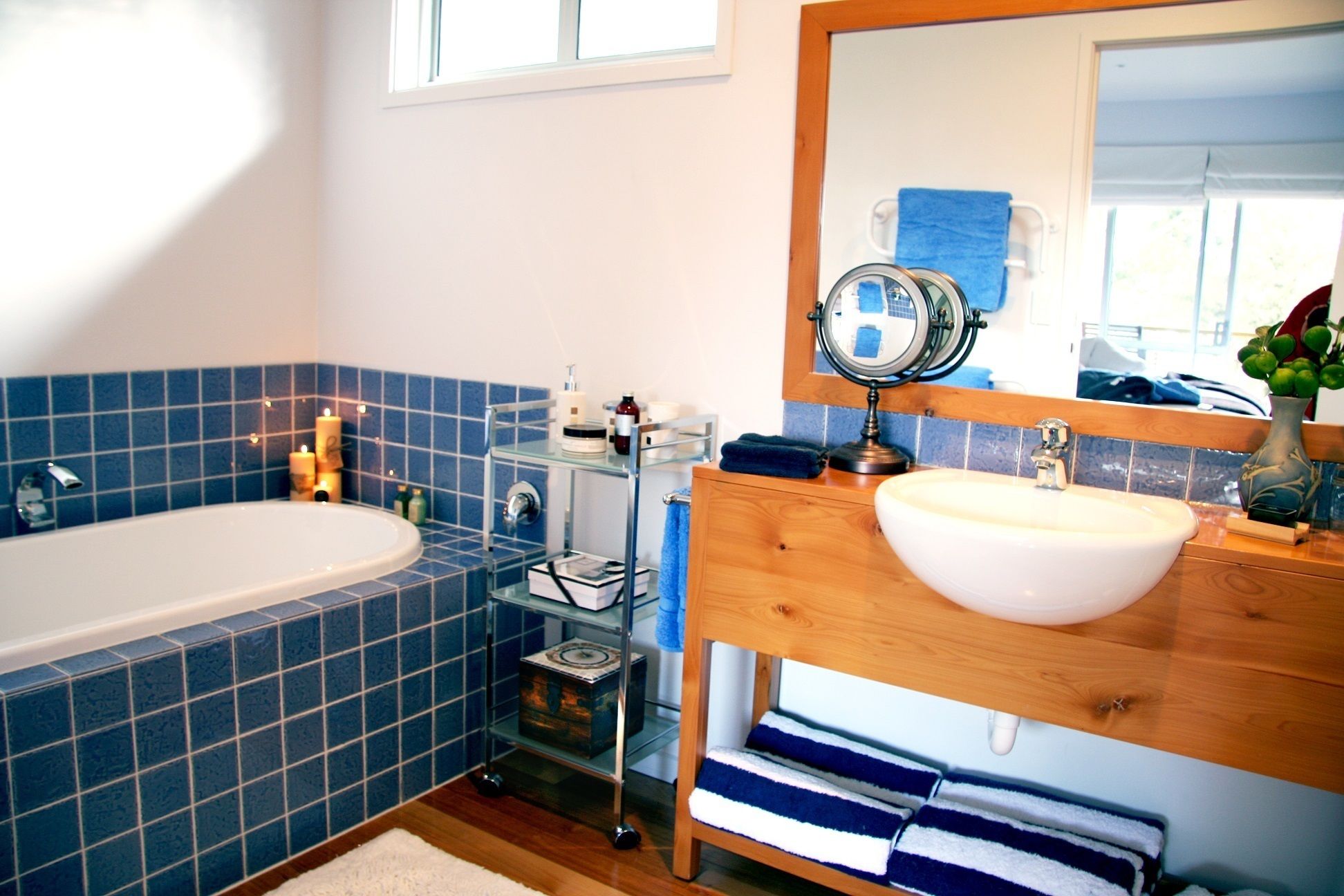 A bathroom with a bathtub, a wooden vanity with a sink, a mirror, and a blue-tiled wall.