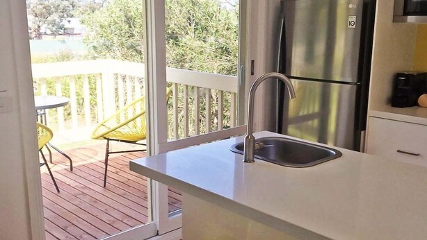 A kitchen with a stainless steel refrigerator, a sink, and a view of a wooden deck with chairs. - Yarra Glen Racecourse Apartments (Yarra Glen)