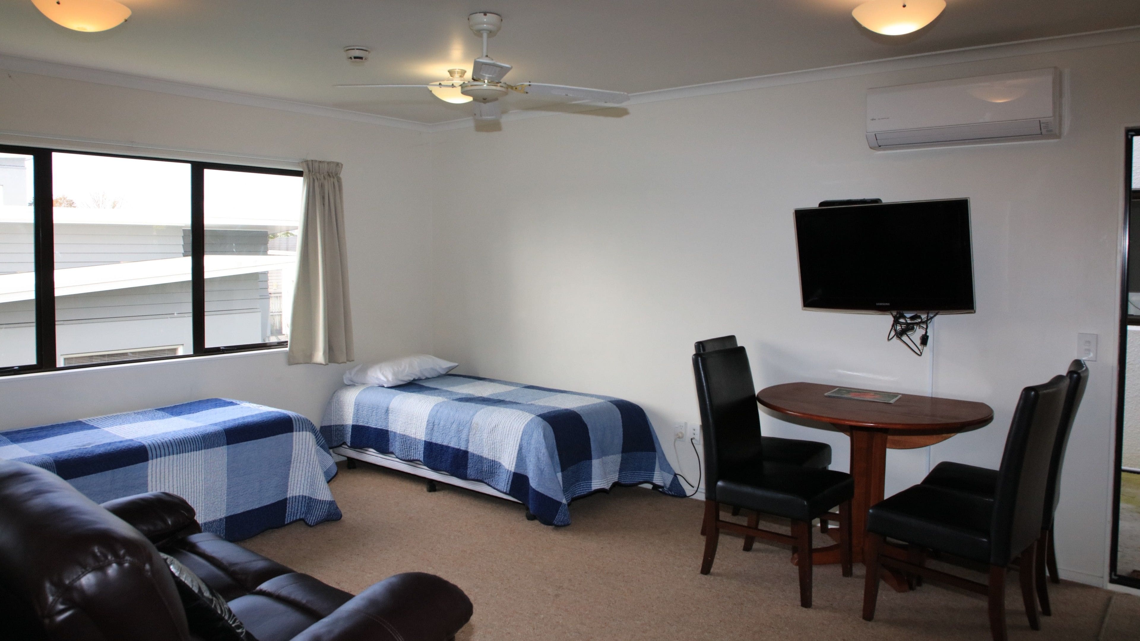 A room with two beds, a TV, a table with chairs, and a ceiling fan.
