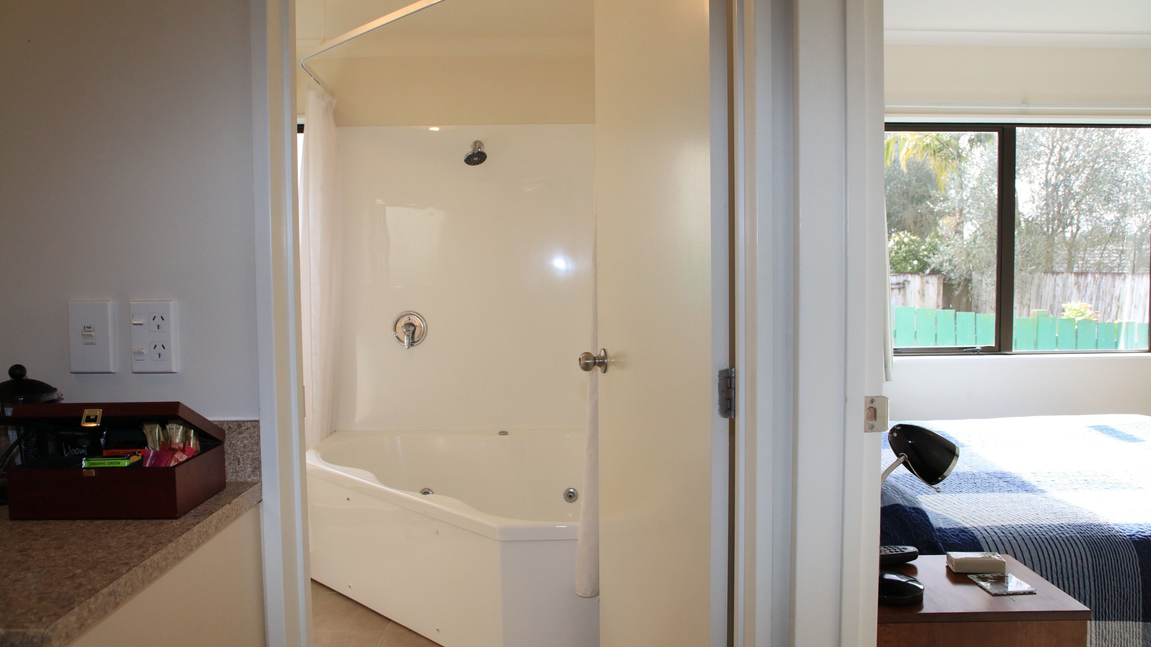 A bathroom with a bathtub, a shower, and a toilet. There is a window with a view of trees and a fence.