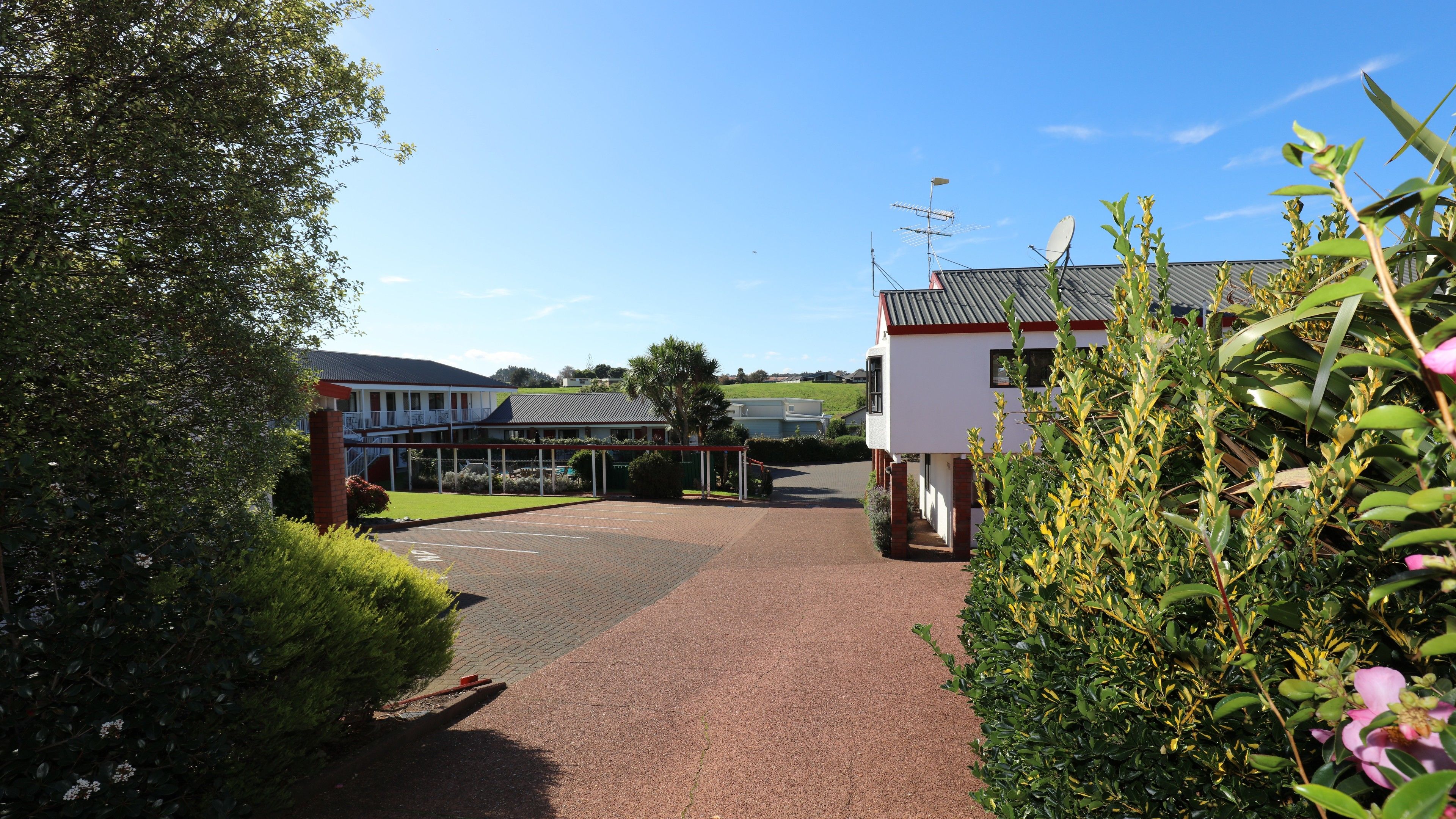 A pathway leading to a building with a satellite dish and a small structure with a red roof.