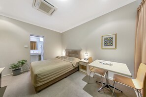 A hotel room with a bed, bedside table, chair, desk, and a potted plant. - Cessnock Motel (Cessnock)