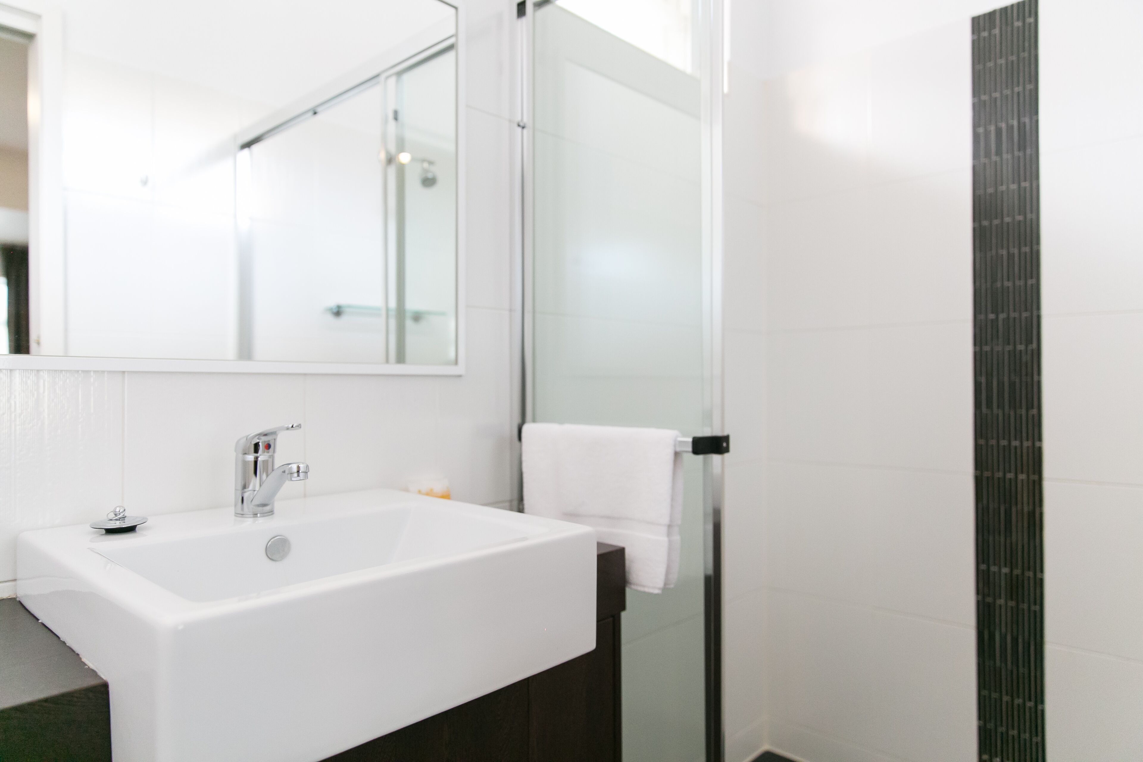 A modern bathroom with a white sink, a mirror, and a glass shower enclosure.