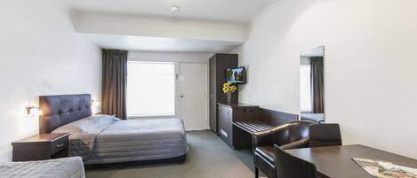A hotel room with a bed, a desk, a chair, a television, and a mirror.