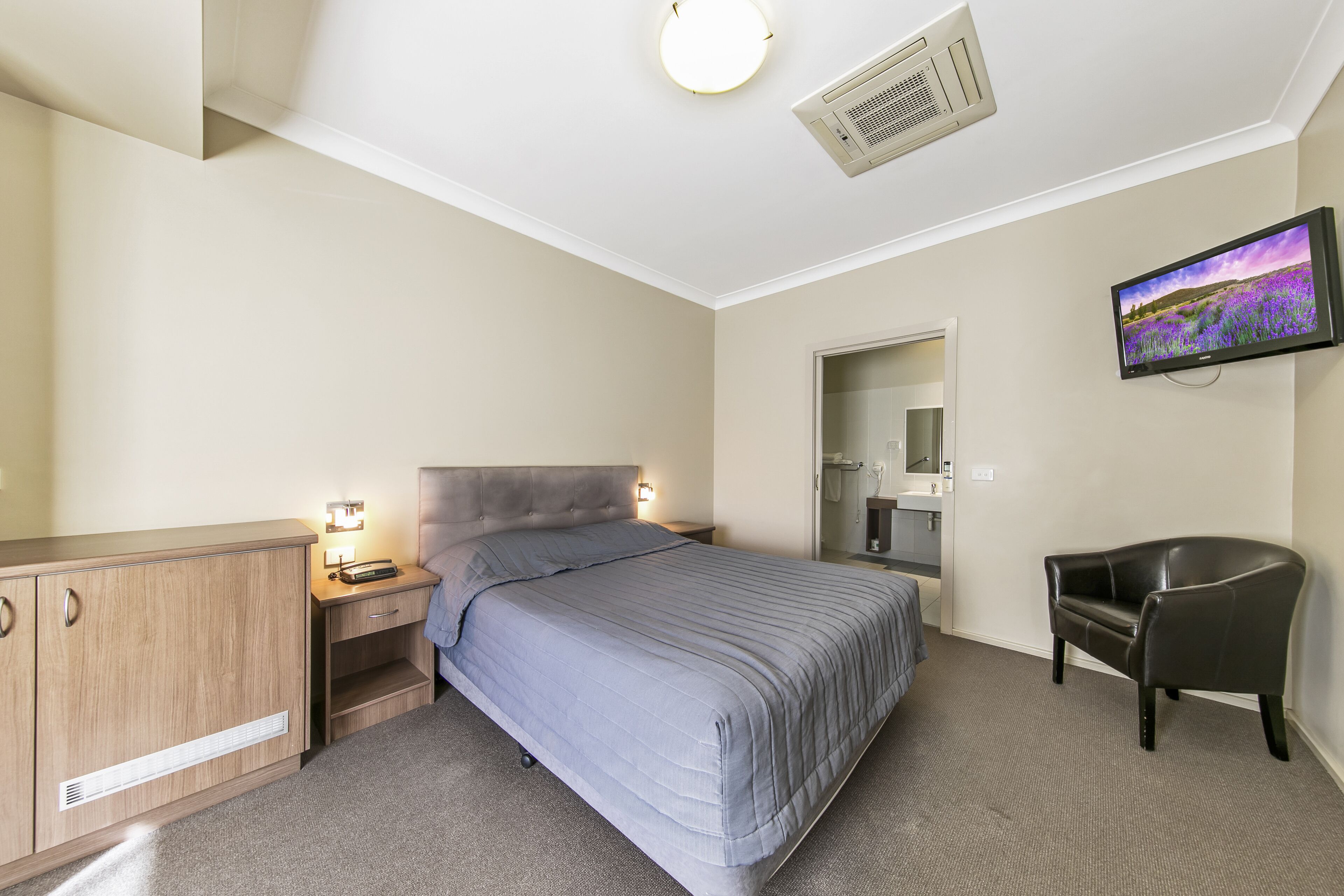 A bedroom with a bed, a desk, a chair, a television, and a bathroom.