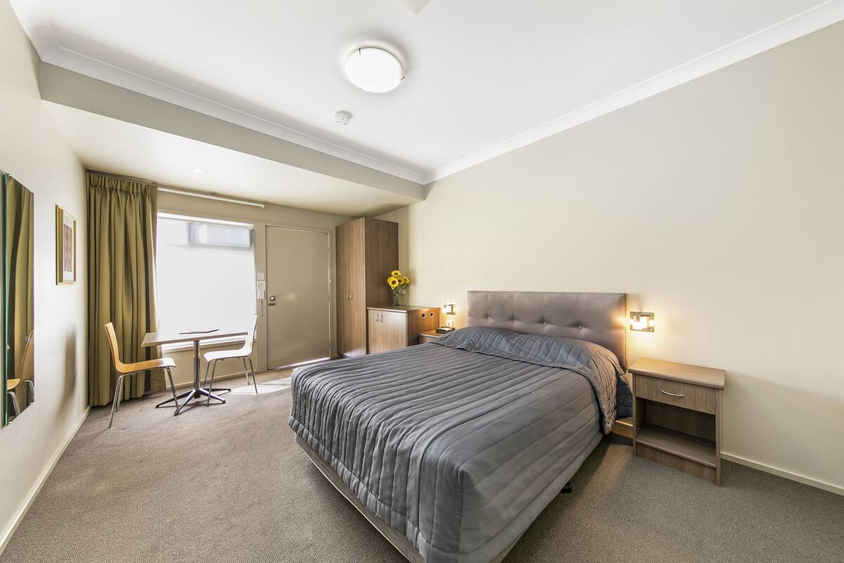 A modern hotel room with a large bed, a desk, a chair, and a small table.