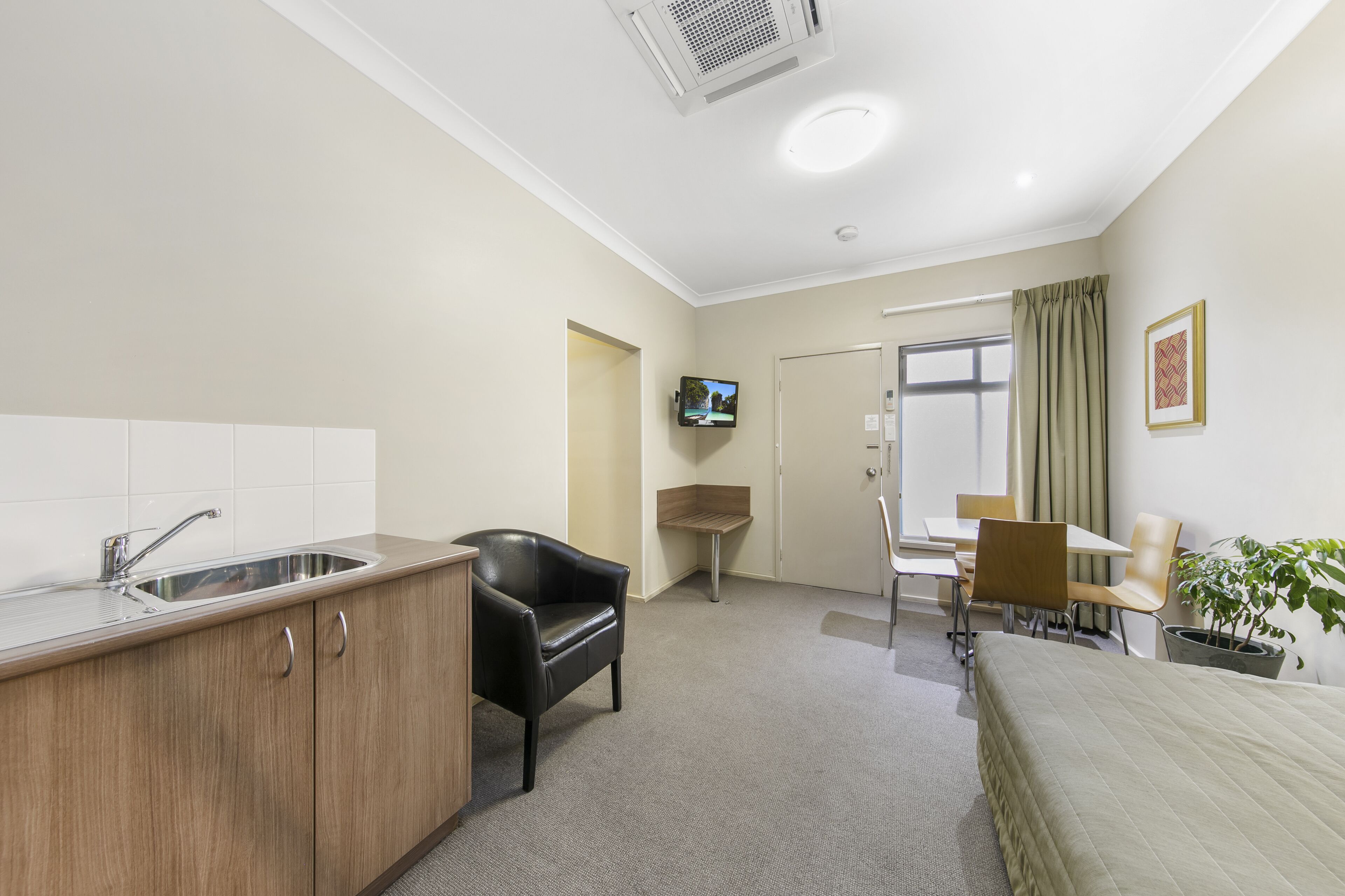 A hotel room with a kitchenette, a bed, a desk, and a chair.