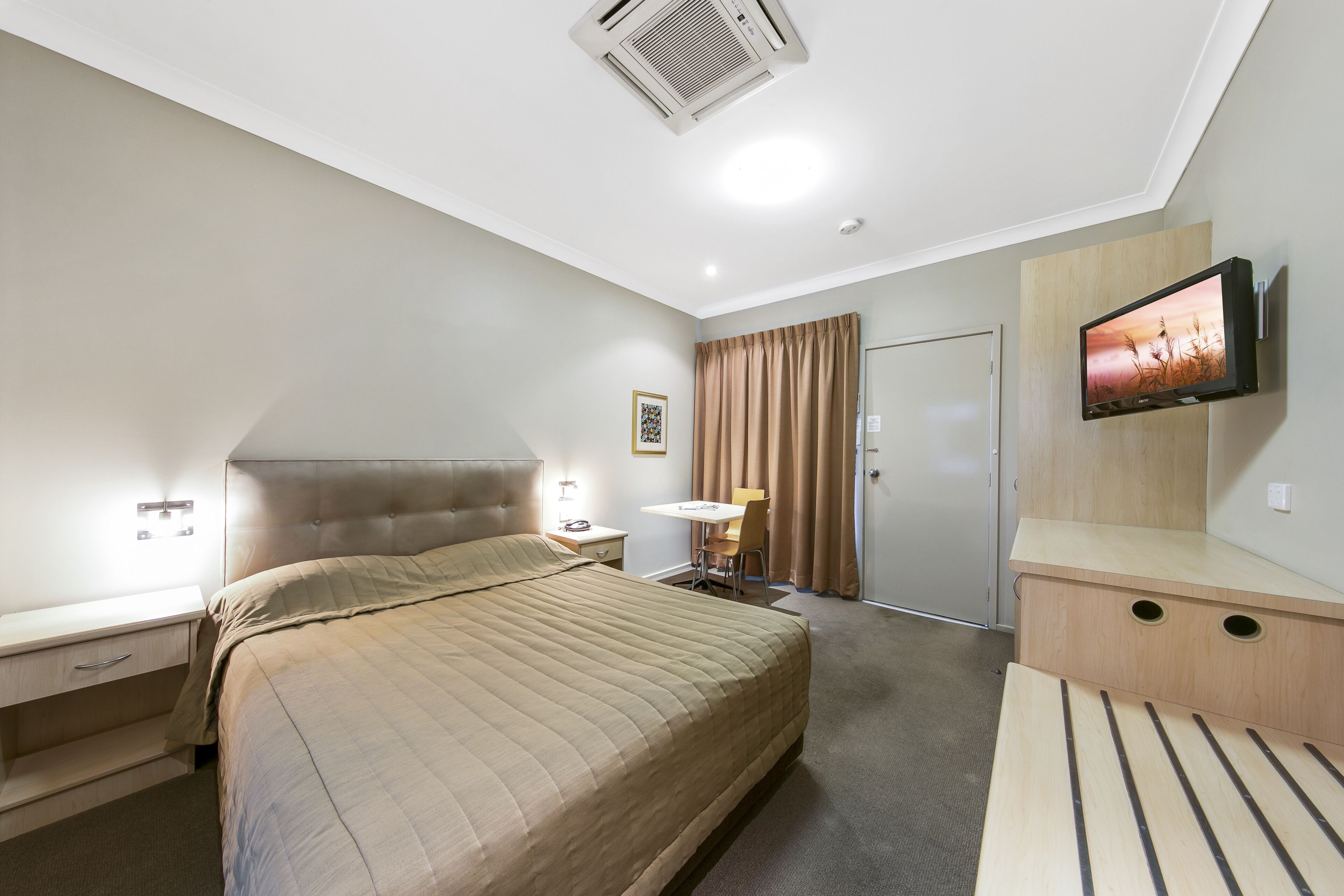 Une chambre d’hôtel comprenant un lit, une table de chevet, une lampe, une télévision et un bureau avec une chaise.